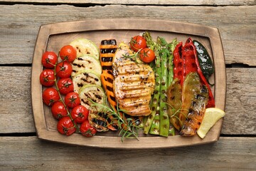 Delicious grilled vegetables and chicken breast on wooden table, top view