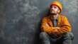 © Andrii - Construction worker in orange hard hat reflects while sitting against a gray wall