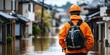 © Kamonwan - A man in an orange jacket stands in a flooded street, surveying the damage and reflecting on the impact of natural disasters.