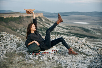 Wall Mural - Woman reading book while sitting on mountain top with legs up in the air