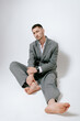 © Elina Leonova - Handsome man in grey suit sits on the floor barefoot