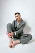 © Elina Leonova - Handsome man in grey suit sits on the floor barefoot