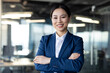 © Liubomir - Confident asian businesswoman in blue suit standing with arms crossed in modern office. Professional appearance, smiling expression, conveys success.
