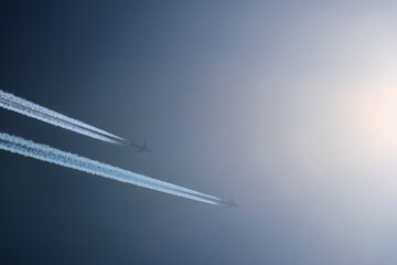 Wall Mural - Two planes are flying towards the sun. Airplanes in the blue sky. Airplane with contrail.