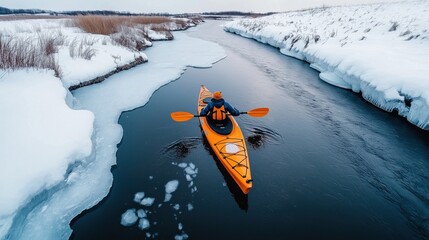 Canvas Print - Person kayaking on a partially frozen river surrounded by snow-covered terrain and icy banks during winter