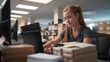 © angel_nt - A young woman diligently types on her computer in a busy office environment filled with stacked boxes. She appears focused and organized as she completes her tasks