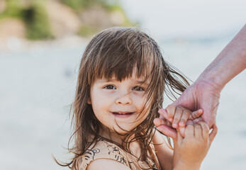 A little girl holds her mother's hand tightly as she looks straight into the camera.