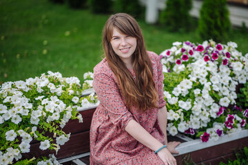 Lovely young lady with flowing hair relaxes in a garden, encompassed by white and purple petunias, savoring the summer