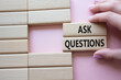 © Natallia - Ask Questions symbol. Wooden blocks with words Ask Questions. Businessman hand. Beautiful pink background. Business and Ask Questions concept. Copy space.