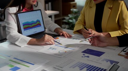 Wall Mural - Businesswomen collaborating in an office setting analyze financial data while pointing at charts on paper. Their teamwork emphasizes effective communication and strategic planning