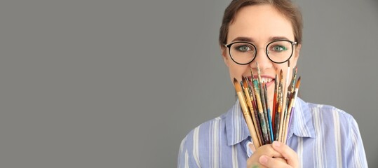 Wall Mural - Young female artist holding many brushes on grey background with space for text