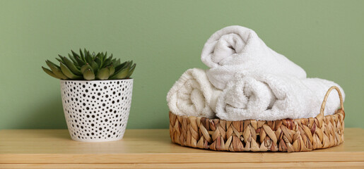 Canvas Print - Wicker basket with towels and houseplant on wooden table in bathroom, closeup