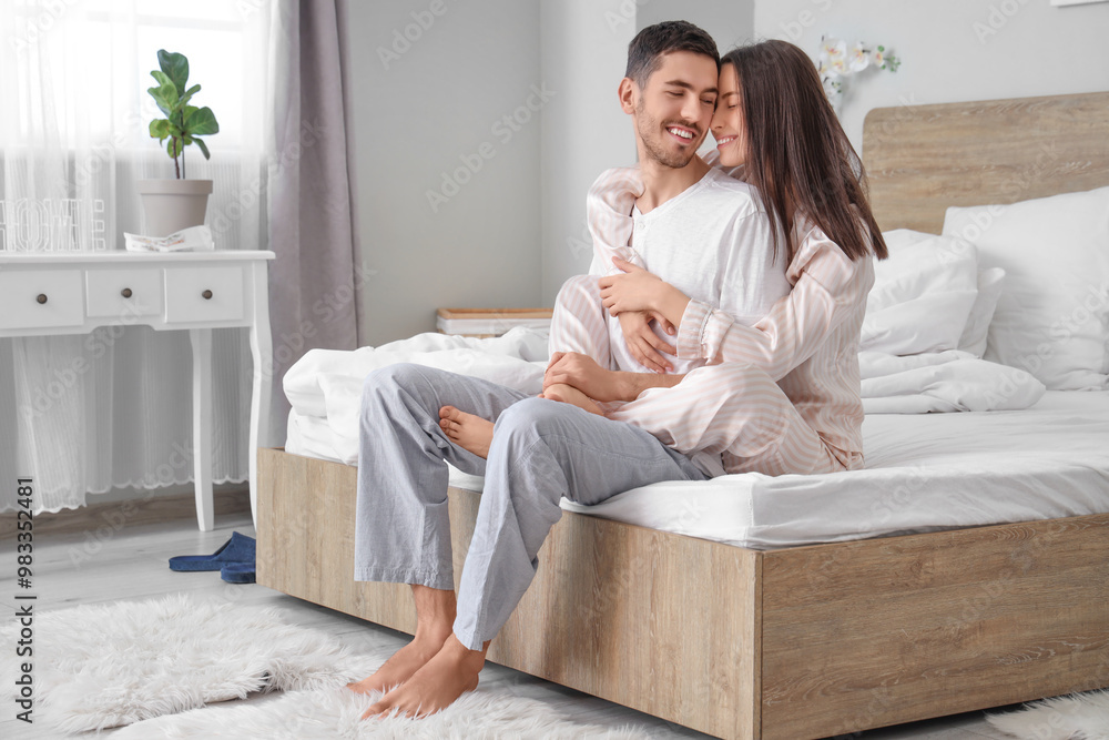Happy hugging young couple sitting on bed