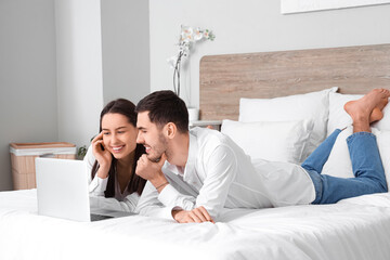 Poster - Young couple lying with laptop on bed