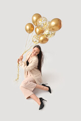 Wall Mural - Happy young woman with air balloons sitting on grey background