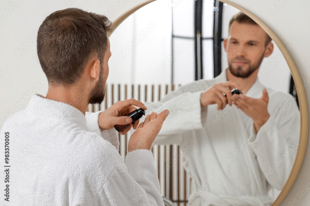 Handsome young man applying essential oil for beard in bathroom
