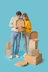 Canvas Print - Beautiful young couple holding cardboard box with tasty pizza on blue background