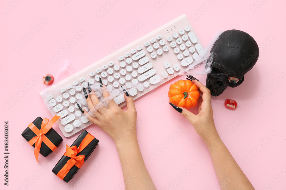 Witch's hands with computer keyboard, gifts and decorations for Halloween on pink background, closeup