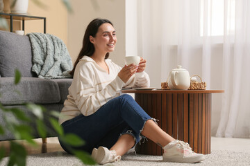 Canvas Print - Young woman with cup of tea sitting on carpet at home