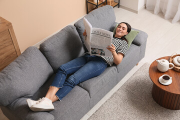 Poster - Young woman reading newspaper on sofa at home