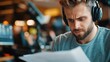 © Lens Legacy - A man wearing headphones displays a serious expression as he reads a script in a lively recording studio, which is equipped with modern digital audio tools.