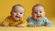 © fourtakig - Twin babies in matching onesies having tummy time on yellow backdrop