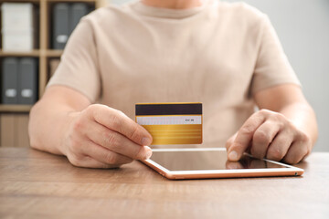 Canvas Print - Man with credit card using tablet at wooden table indoors, closeup