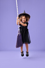 Wall Mural - Funny girl with broom dressed like witch for Halloween celebration on violet background