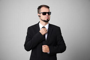 Wall Mural - Young bodyguard in suit and sunglasses on grey background