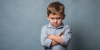 © Sandra - Angry little boy stands with arms crossed, upset face scrunched in frustration, gazing directly at camera, conveying tantrum-like emotion in a studio setting.
