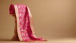 © P.G - A traditional Banarasi sari in bright pink and gold, draped on a plain wooden stand, simple beige backdrop.