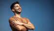 © Hathairat - A cheerful young man smiles widely against a blue background, showcasing joy and confidence with crossed arms.