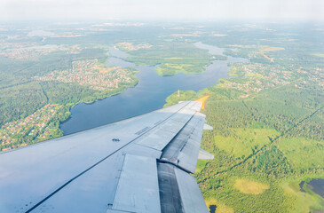 Wall Mural - View of airplane wing, blue skies and green land during landing. Airplane window view.