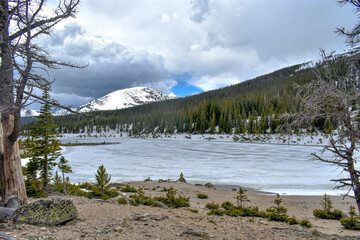 Person sitting at edge of frozen lake, Sandbeach Lake, Rocky Mountain National Park, Colorado