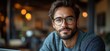 © MaMaKe - A young man with a beard and glasses looks thoughtfully at the camera while sitting in a cafe.