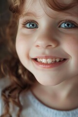 A little girl smiling brightly, with a clear focus on her happy expression and blue eyes.