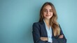 © Alpa - Happy young blonde businesswoman in suit standing with crossed arms and looking at camera on light blue background