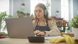 © Krakenimages.com - A focused young woman using a laptop at a well-lit desk with headphones, showcasing remote work in a modern home environment.