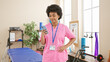 © Krakenimages.com - African american woman healthcare professional in pink scrubs using smartphone indoors at a rehab clinic.