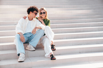 Canvas Print - Smiling beautiful woman and her handsome boyfriend. Couple in casual summer clothes. Happy cheerful family. Female and man having fun. They posing in the street in sunny day. Sit at stairs