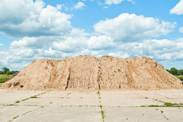 a mountain of sand against a blue sky and clouds