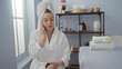 © Krakenimages.com - Woman, young, beautiful, caucasian, speaking on the phone, wearing a white robe, holding a paper, sitting in a relaxing spa setting with candles, towels, and flowers