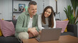 © Krakenimages.com - A smiling couple sitting on a couch in their living room and looking at a laptop screen together