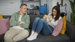 © Krakenimages.com - A woman using a smartphone with a disinterested man sitting beside her on a sofa in a modern living room.