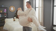 © Krakenimages.com - Man playfully lifting woman in a cozy, modern bedroom, exemplifying joy and affection between a couple.
