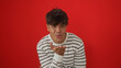 © Krakenimages.com - Young, attractive hispanic man wearing a striped shirt blowing a kiss, isolated against a vibrant red background.