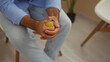 © Krakenimages.com - A young hispanic man sits indoors in a waiting room, gripping a stress ball tightly with both hands, wearing light clothing and appearing thoughtful.