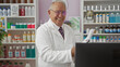 © Krakenimages.com - Smiling elderly man in white lab coat working in a pharmacy store, surrounded by various health products and medicines on shelves.
