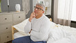 © Krakenimages.com - Thoughtful middle-aged man with grey hair in bedroom, sitting on bed, looking up pensively indoors.