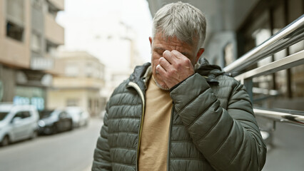 Poster - A grey-haired man appears distressed on a city street, covering his face with his hand.